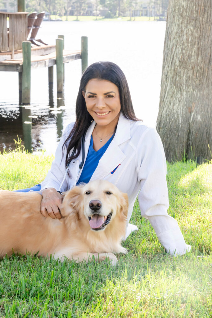 Vetzi veterinarian crouching with golden Labrador outdoors by waterfront.